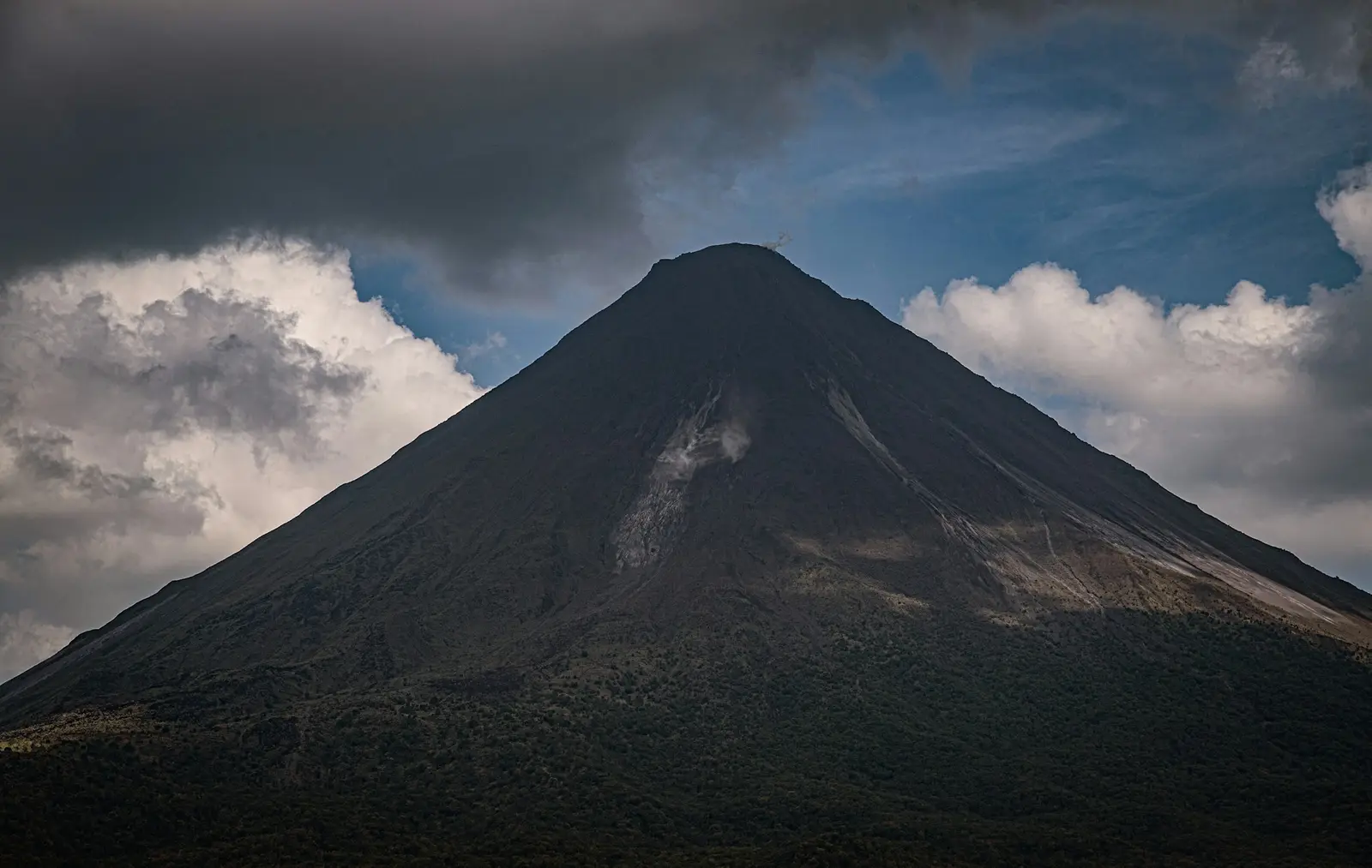 Arenal Volcano rising above forest under a cloudy sky in Costa Rica